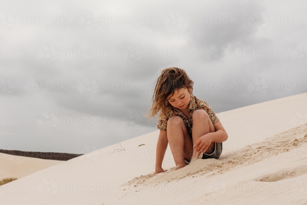 Boy sitting on a sand dune and playing with the sand - Australian Stock Image