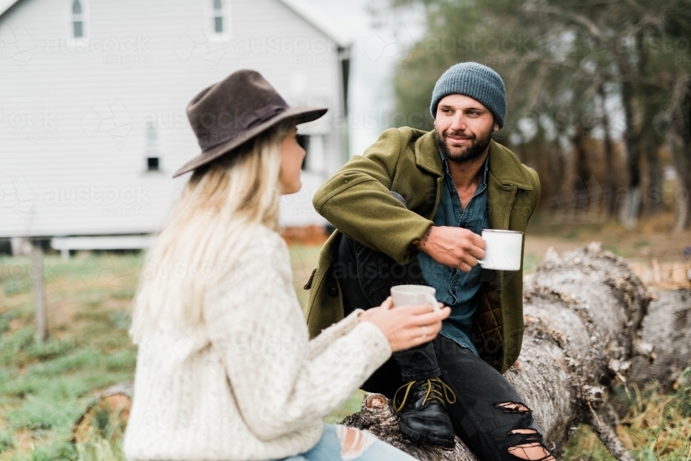 Couple sitting on fallen tree, talking and drinking coffee - Australian Stock Image