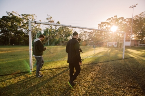 3 men walking on the field near the soccer net during sun set