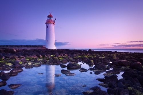 A lighthouse reflecting in rockpools below a coloured sky before sunrise