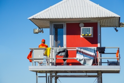 A surf lifeguard sitting in a watch tower with a corrugated tin roof.
