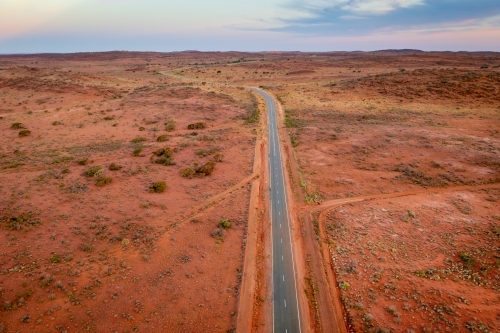 Aerial view of a bitumen road running through and arid outback landscape at twilight