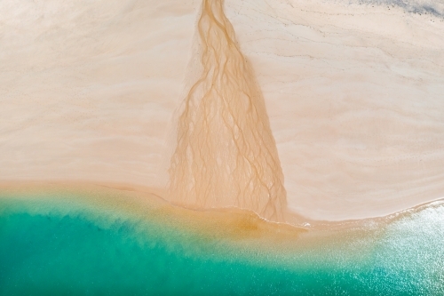 Aerial view of a small creek flowing over a white sandy beach into the sea