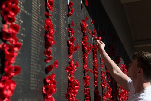ANZAC DAY at the Australian War Memorial, man placing poppy next to name on wall of remembrance