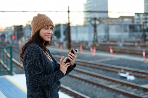 Asian woman waiting at train station holding mobile phone