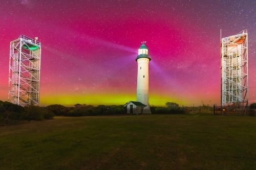 Aurora Australis filling the night sky over a tall lighthouse and nearby navigation towers