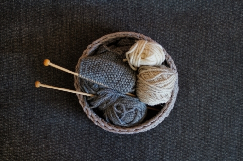 Basket of knitting, knitting needles and wool on grey background