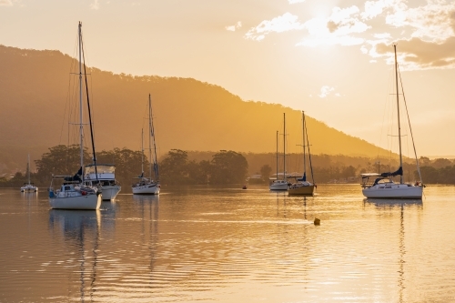 Boats and yachts moored on a still river in front of golden sunset