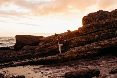 Boy climbing on rocks at sunset