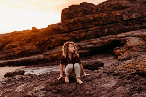 Boy sitting on rocks at the ocean at sunset