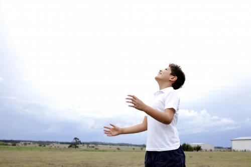 Boy throwing ball up into air, looking up at sky