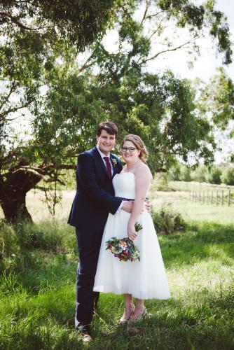 Bride and Groom standing beside a tree in paddock looking at camera