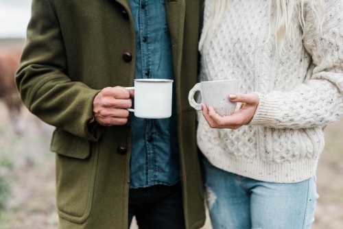 Close up of couple holding cups of coffee outside on farm