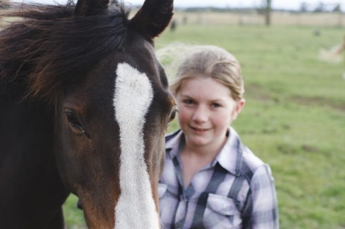 Close up of young girl standing beside horse in paddock