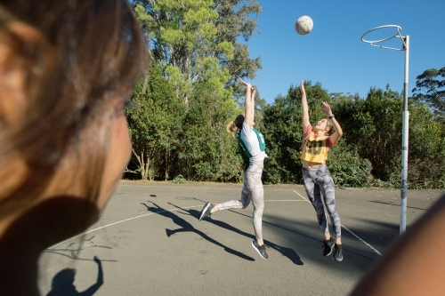 close up shot of a woman watching two young women jumping in mid air playing net ball