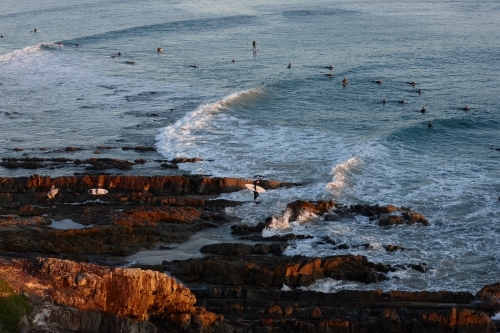 Surfers surfing off at coastal headland on sunrise