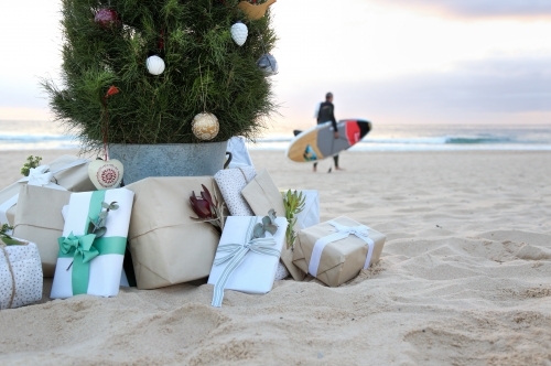 Decorated Christmas tree with presents at beach with surfer in background