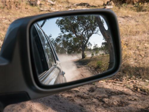Dirt road and dust in the rear vision mirror of a car