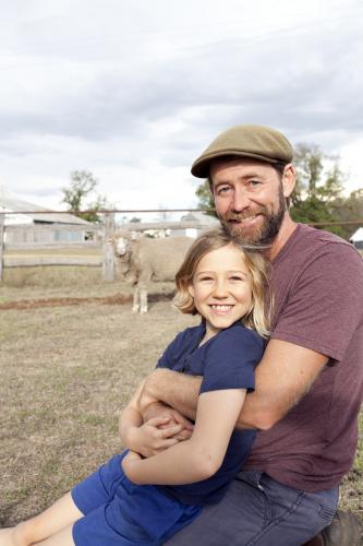 Father hugging daughter on farm with sheep in background