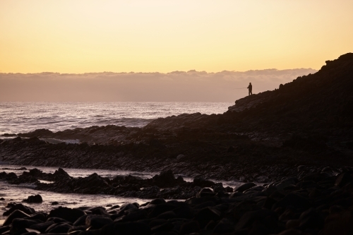 Fisherman fishing in coastal landscape on sunrise