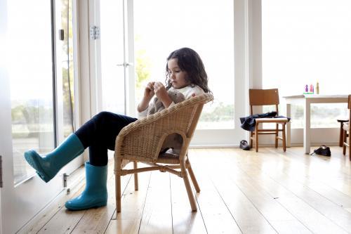 Girl wearing blue gumboots sitting inside on a wicker chair
