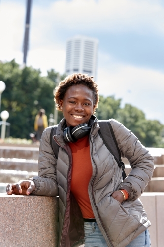 Happy young African woman wearing wireless headphones in city