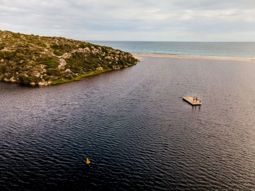 horizontal photo of an island and the ocean with three people standing on a floating wooden raft