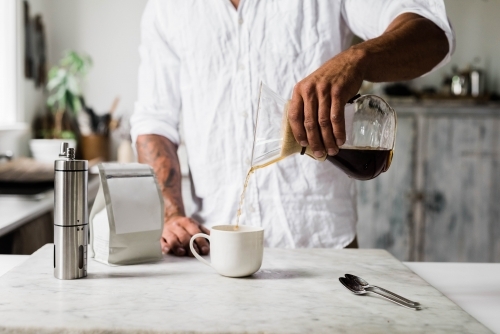 Horizontal shot of a man pouring coffee into  a cup