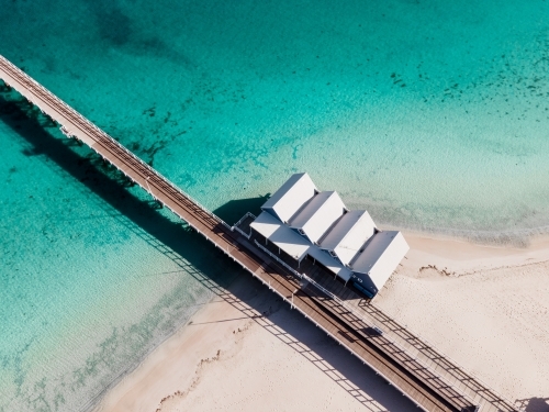 horizontal shot of four beach houses with walkway with clear blue and green waters and white sand