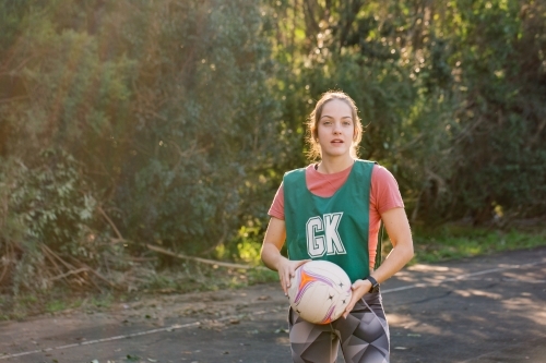 horizontal shot of young woman in sports clothes holding a net ball with two hands on a sunny day