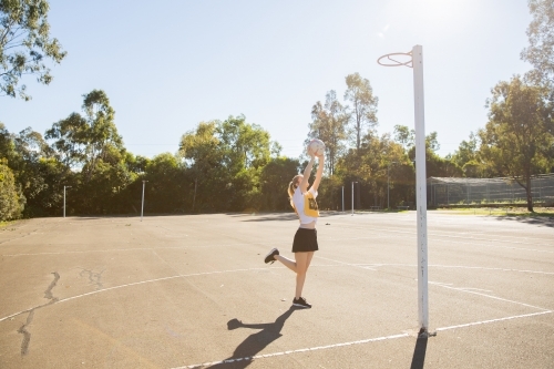 horizontal shot of young woman in sporty clothes throwing a net ball in the air with one foot raised