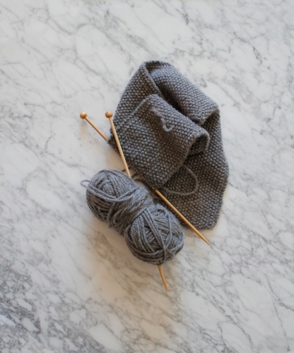 Knitting with wooden knitting needles with grey wool on marble
