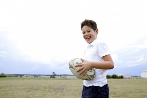 Laughing boy holding football outside