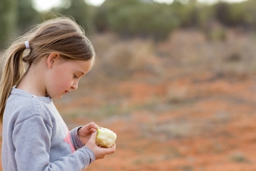 Little girl with apple outside with red dirt