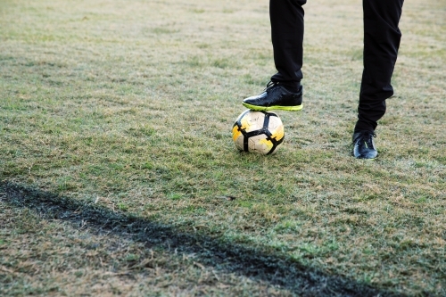 Lower body extremity shot of a man standing on the field stepping on a soccer ball with one foot