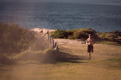 Male exercising on a morning run beside the ocean