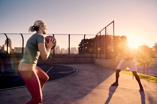 Man and woman passing basketball in sunlight