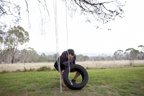 Man making a tyre swing in country backyard