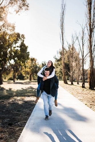 Man running carrying girlfriend piggy back laughing on path in park