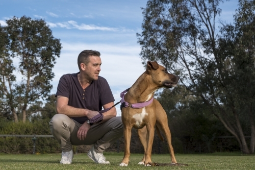 Man Squatting in Park next to Crossbreed Dog