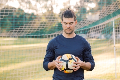 man standing on the field while looking down holding a soccer ball
