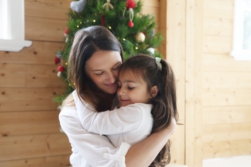 Mother and daughter hugging with Christmas tree in background