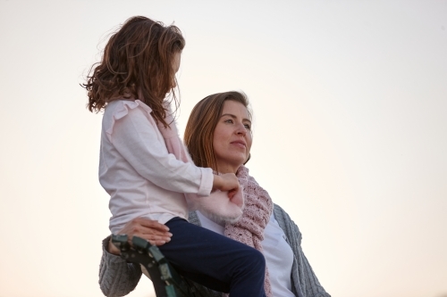 Mother and daughter sitting on park bench at park on sunset