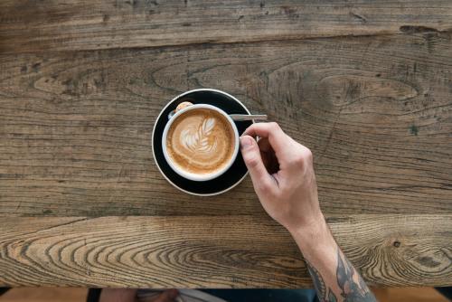 Overhead image of a coffee on a wooden table with customer's arm