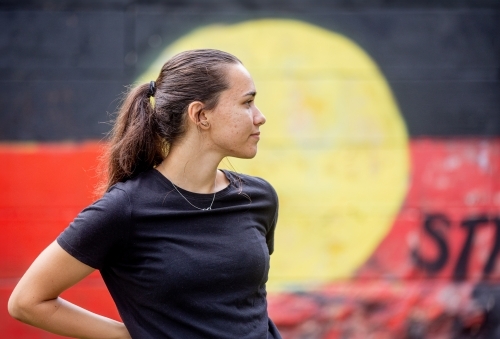 Portrait of an Aboriginal woman standing with a red, yellow and black flag mural in the background
