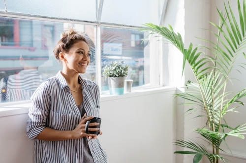Relaxed female employee standing with a cup of coffee by the window