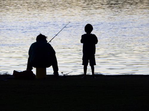 Silhouette of fisherman and boy at water's edge