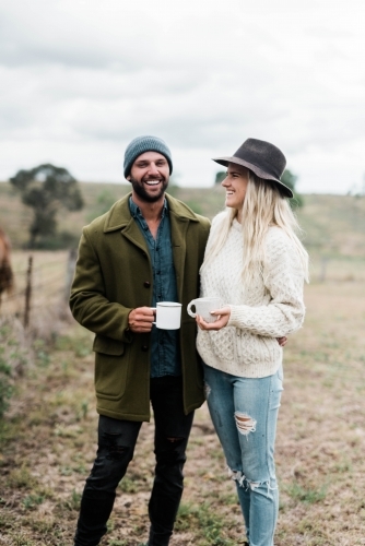 Smiling couple on farm holding coffee cups