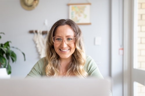 Smiling woman with green blouse wearing an eyeglass while looking at a laptop screen