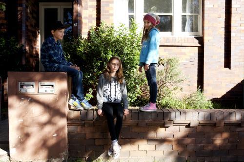 Three kids on the brick wall outside their urban house